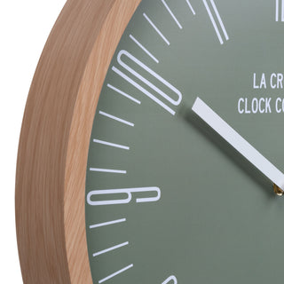 Close-up image of the frame and dial detail of the 404-3041D 16-inch Ellwood Wall Clock, featuring a flush-mount light wood frame, a sage green dial, modern white numbers, and white metal hour and minute hands.
