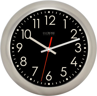 A round wall clock with a brushed silver metal frame, a black face, large off-white Arabic numerals, silver hands, and a red second hand. The brand name 'LA CROSSE CLOCK CO.
