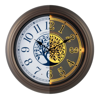 Head-on image of the 403-3246BR Lux lighted indoor outdoor wall clock with a center image of a tree and Arabic numbers on a white and blue dial surrounded by a brown frame, showing half the clock with the light and the other half without the light