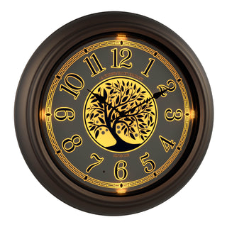 Right-facing lighted dial of the 403-3246BR Lux lighted indoor outdoor wall clock with a center image of a tree and Arabic numbers on a white and blue dial surrounded by a brown frame displaying the backlight glow function