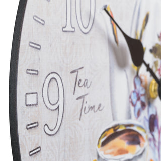 Close-up detail image of the MDF construction of the 404-2631T 12-inch Teatime Wall Clock. The clock features an image of a floral teapot and teacup on a light-textured background, with the text "Tea Time," white numbers, black metal hands, and an open face design.
