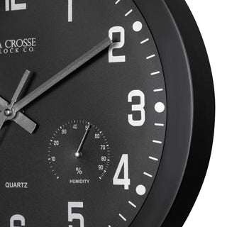 Detailed image of the frame of the 404-2631 12-inch Inkwell Wall Clock with a black flush mount frame surrounding a black dial with white numbers, thermometer that reads both Fahrenheit and Celsius, and a Humidity gauge, featuring silver metal hour, minute, and second hands