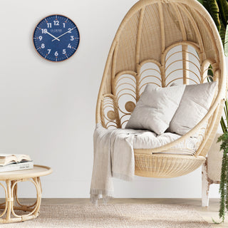 Lifestyle image of the 404-3027C Portside eleven inch navy blue wall clock with white numbers, orange time markings, and a copper case featuring white hour and minute hands in a nautical themed room