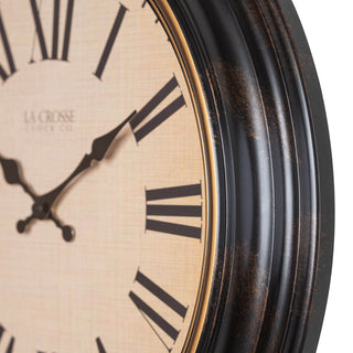 Left facing close-up of the frame and dial of the 404-3045BK 18-inch Traditions Wall clock featuring a dark decorative frame with bronze bezel surrounding a linen detailed dial with black Roman numerals and metal decorative hands