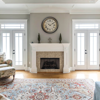 Traditional decor living room with the  404-3045BK 18-inch Traditions Wall clock featuring a dark decorative frame with bronze bezel surrounding a linen detailed dial with black Roman numerals and metal decorative hands hanging above a white mantel fireplace between two sets of French doors