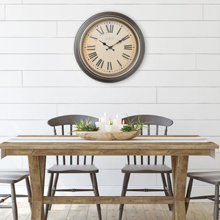 Farmhouse Chic style dining room with  the 404-3045BK 18-inch Traditions Wall clock featuring a dark decorative frame with bronze bezel surrounding a linen detailed dial with black Roman numerals and metal decorative hands hanging on the white shiplap wall above a rustic wood table and black farmhouse chairs