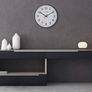Modern interior design room with a shelf holding decorative vases and a light with a La Crosse Clock 19-inch commercial clock on the dark gray textured wall.