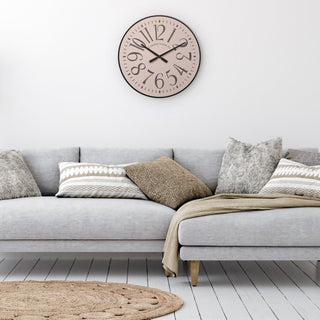 404-3053 A round wall clock with a black frame and beige face hangs above a light gray sofa with patterned throw pillows and a beige blanket in a bright, modern living room.
