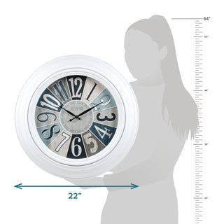 404-3056 A round wall clock with a white frame and a distressed multicolor dial in shades of blue, gray, beige, and black. The image includes a woman's silhouette showing the clock's height and width measurements, with blue arrows indicating 22 inches wide by 64 inches tall.