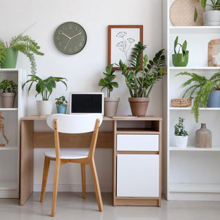 Lifestyle image of the 404-3831G 12-inch Paxton Wall Clock - Green, with Silent Sweep, shown hanging on a wall in a home office with a desk, bookshelves, and plants. The clock features a flush-mount green frame, a matching color dial, brass raised numbers, and brass-finished hour, minute, and second hands.