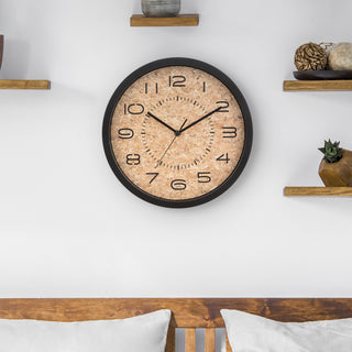 Lifestyle of the 12-inch 404-3832 Felix Cork Wall Clock with laser cut numbers and time markings with black hour, minute, and second hands hanging above a wood bedframe with white pillows on a white wall with wooden shelves