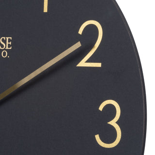 Black clock face with gold numbers and brand name