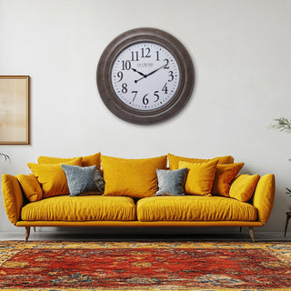 404-4292 A round wall clock with a dark brown wood-look frame and white face hangs above a mustard yellow velvet sofa with gray and yellow pillows in a living room setting.