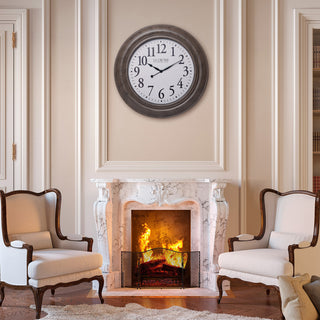 404-4292 A round wall clock with a dark brown frame and white face hangs above a marble fireplace mantel with a burning fire. Two cream-colored armchairs sit on either side in a classic room setting.