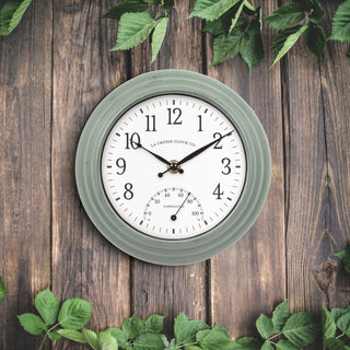 Green wall clock with white face on a wooden background with green leaves.