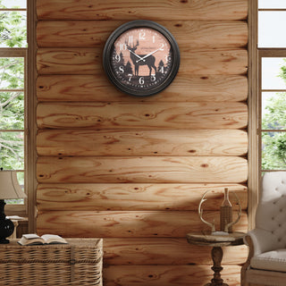 A round wall clock with a black frame and a rustic wood-grain face featuring a deer silhouette, mounted on a light wood log wall in a cozy room setting.