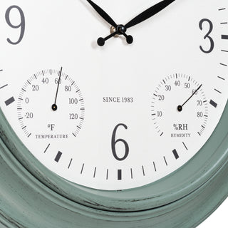 Close-up of a wall clock face with a distressed sage green frame, white dial, black numerals, and two subdials showing temperature in Fahrenheit and humidity in percent relative humidity. The text 'SINCE 1983' is printed on the dial.