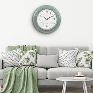 Gray sofa with patterned cushions and a green blanket, clock on the wall above.