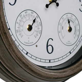 Close-up of a round wall clock with a white dial, black numerals, two small gauge dials, and a dark wood-toned outer frame.