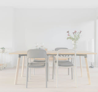 A modern dining table set in a minimalist dining room. The table has a light natural wood top and angled light wood legs, surrounded by three chairs: two with black woven seats and backs, and one with a white metal frame.