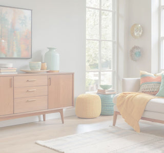A styled mid-century modern living room featuring a wooden sideboard cabinet, a yellow knit pouf, a teal side table, a mustard yellow throw blanket on a sofa, and a large framed abstract painting on the wall.