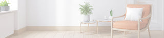 A modern orange-brown upholstered armchair with a white pillow, set in a bright room next to a small round side table and a potted plant.