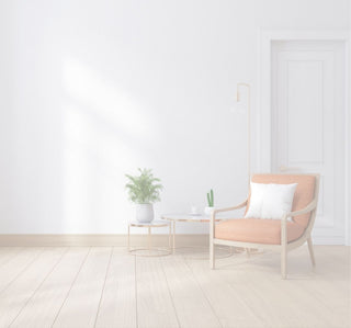 A modern orange-brown upholstered armchair with a white pillow, set in a bright room next to a small round side table and a potted plant.