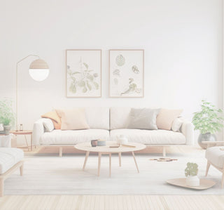 A bright, modern living room featuring a light beige sofa with black and white accent pillows, a round coffee table, a large white area rug, a floor lamp, and a potted plant.