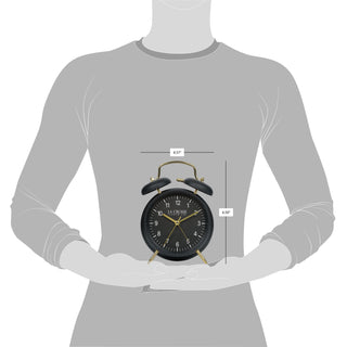 Dimension image of the W72449 Metal Twin Bell Alarm Clock – Black, the clock features a black dial with white numbers, gold hands and accents, in a black metal case. The dimensions read 4.57 in wide and 6.50 in tall.